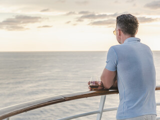 Stylish man with a glass of drink standing on the empty deck of a cruise ship against the backdrop of sea waves. Sunny day. Chill lifestyle, luxury travel. Perfect for holiday and travel themes © Svetlana