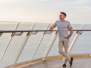 Fashionable man with a glass of drink standing on the empty deck of a cruise ship against the backdrop of sea waves. Sunny day. Chill lifestyle, luxury travel. Perfect for holiday and travel themes © Svetlana