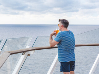 Fashionable man with a glass of drink standing on the empty deck of a cruise ship against the backdrop of sea waves. Sunny day. Chill lifestyle, luxury travel. Perfect for holiday and travel themes © Svetlana
