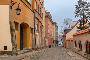 Obraz premium Quiet old town street with worn plaster facades, arches and lanterns along a curved cobblestone road in a calm European urban atmosphere