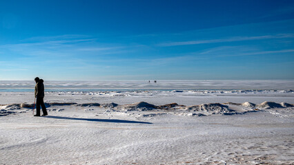 Wonderful view of the frozen sea coast in winter, man walks along the snowy seashore, rocky coast
