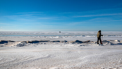 Wonderful view of the frozen sea coast in winter, man walks along the snowy seashore, rocky coast