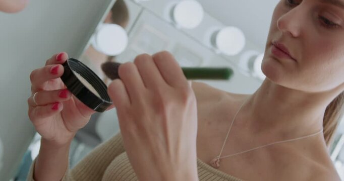 Close-up of a caucasian girl as a makeup artist applies makeup powder on a client face.