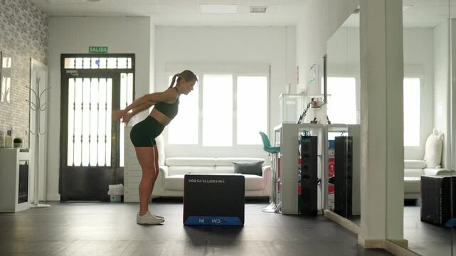 Athletic woman performing box jump exercise in gym