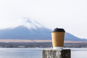 Takeaway paper coffee cup on a wooden post with blurred Mount Fuji in the background.