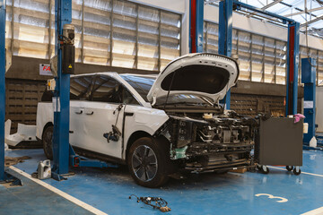 Modern white electric vehicle with side damage in a professional repair service center.