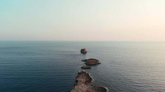 Rocky islet emerging from the calm mediterranean sea at cala toro, in favignana, aegadian islands, sicily, italy