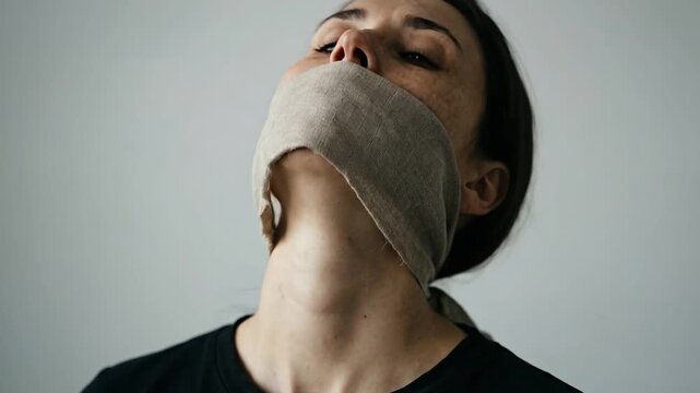 Woman with mouth covered looks up and down, portraying struggle and constraint