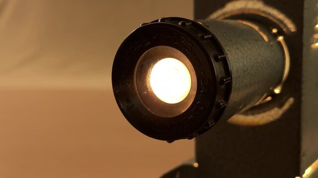 A vintage film projector whirs as it feeds a celluloid strip through its lens. The soft, warm glow from the machine creates a nostalgic and peaceful atmosphere in the dim room.