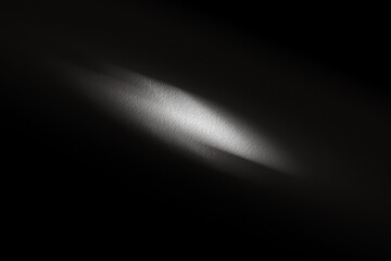 Soft light beam illuminating textured surface in dark environment, creating subtle shadows and highlights, emphasizing the contrast between light and dark areas