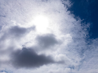 Obraz premium Sun illuminating a partly cloudy sky with dense grey clouds and wispy altocumulus revealing a patch of clear blue sky and rays breaking through toward the horizon