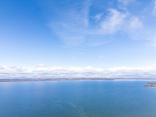 Vast blue waters of lake simcoe stretching towards the distant treed shoreline under a bright blue sky with scattered clouds, showcasing the tranquil natural landscape in georgina, ontario, canada