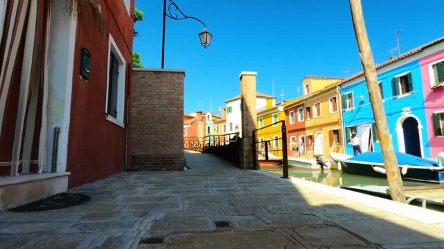 A view along Riva dei Santi and Fondamenta di Terranova footpaths in Burano. Colorful houses and boats moored in the waterway.