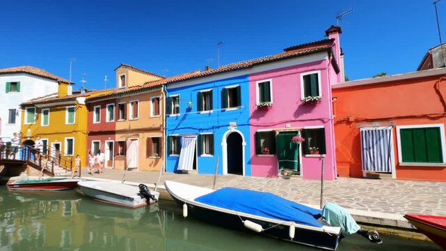 Burano / Venice / Italy - June 23, 2019: WALKING SHOT  A view along Riva dei Santi and Fondamenta di Terranova footpaths in Burano. Colorful houses and boats moored in the waterway.
