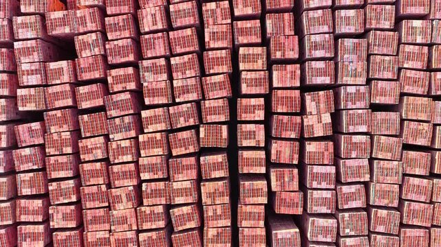 Bird's-eye view of the symmetrical arrangement of red brick pallets. Aerial drone footage of the industrial texture and order in the construction materials warehouse.