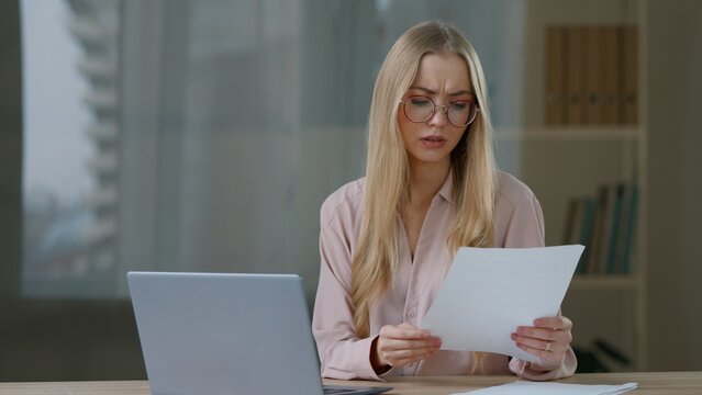 Caucasian business woman with laptop working confused checking paper documents mistake female girl businesswoman manager worker difficult job online with computer and paperwork at table at home office