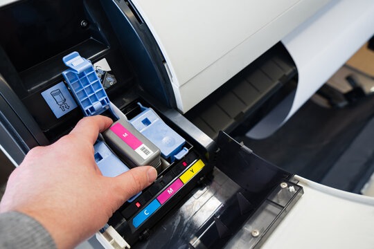 Close-up of a worker's hand changing the magenta ink cartridge inside a professional plotter printer