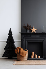 A pleated black paper Christmas tree stands beside textured candles and decorative objects