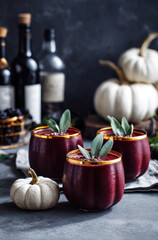 Three glasses of colorful drinks with sugar rims sit on a table surrounded by white pumpkins and sage leaves.