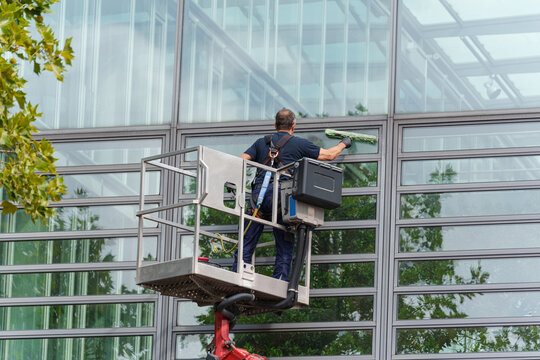 Worker cleaning large glass facade using lift platform outside modern office building