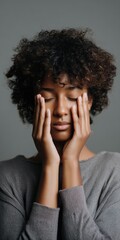 African female adult with curly hair in thoughtful pose on gray background