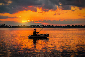 Fisherman in rubber boat catch the fish at sunset