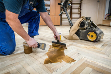 Professional worker fills the gaps cracks of the old wooden parquet with a spatula after sanding. Floor renovation