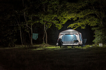 Silhouette of men is resting near illuminated tent in the forest at night