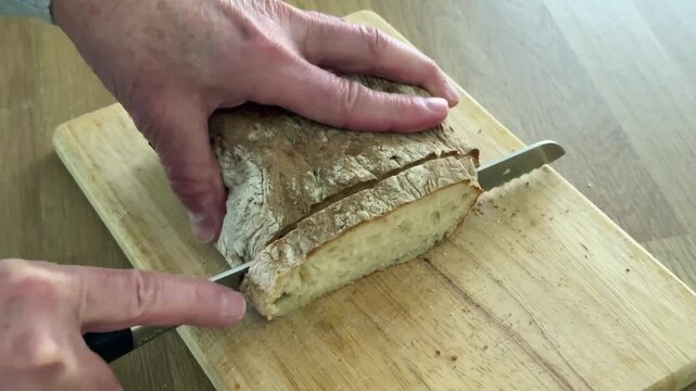 Fresh crusty sourdough bread being sliced with a sharp bread knife on a wooden chopping board in a home kitchen