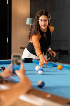 Woman playing billiards with friends taking photo