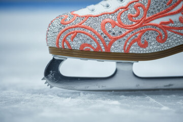 Close up of figure ice skate with silver glitter and orange pattern on frozen rink surface illustrating winter sports, fashion design and holiday performance concepts