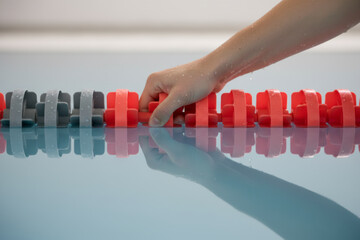 Swimmer hand gripping red pool lane rope with water reflection representing rest after training or finishing race suitable for sports competition banner or swimming club advertisement