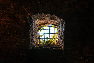 Historic fortress dungeon window with iron bars and strong light beyond, representing captivity, isolation, escape, and contrast between darkness and freedom.