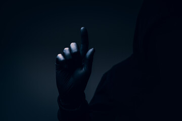 Dark hooded silhouette with obscured face and raised index finger, menacing gesture symbolizing intimidation, warning, fear, and mystery.