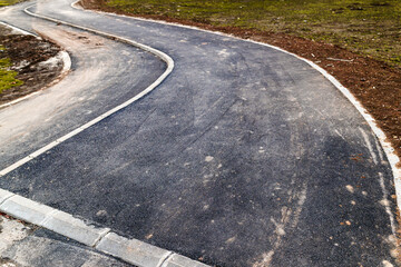 Curved asphalt pedestrian and cycling paths with white border lines in an urban environment, showing modern city infrastructure and mobility design.