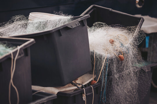 Fish nets and storage boxes are neatly arranged by the harbor. Morning light highlights the delicate threads, showing the tools of a fisherman&rsquo;s trade at a peaceful location