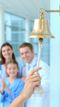 Cancer treatment completion bell in hospital corridor, patient hand pulling rope to ring brass bell, oncology remission milestone, survivor celebration moment, family support nearby