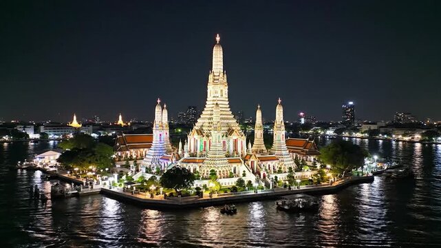 An ornate riverside Buddhist temple illuminated with colorful lights.