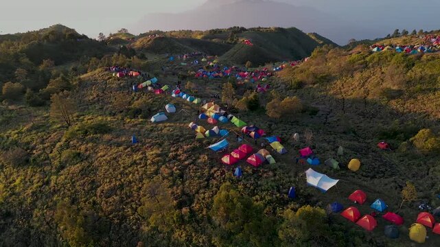 Drone footage of Colorful Tents on Mount Prau hills Savanna at Sunrise. Hikers enjoying calm sunrise moment with breathtaking Sindoro and Sumbing mountain landscape.