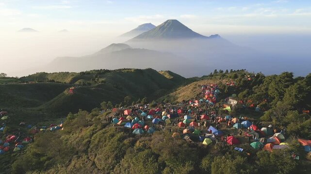 Aerial panorama of peaceful Mount Prau savanna in Central Java. Campers and trekkers experience quiet mountain beauty beneath Sindoro and Sumbing peaks.