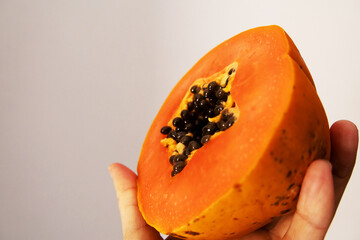 Close-up shot of a vibrant, fresh papaya half held gently in a hand. The bright orange flesh and...
