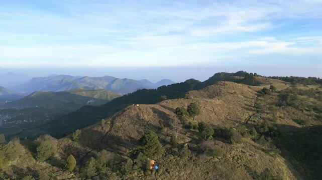 Expansive aerial of Mount Prau hills in Wonosobo. Quiet trekking destination with hikers exploring peaceful grassland and distant volcanic mountain scenery.