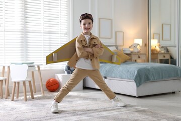 Smiling little boy with cardboard plane wings and goggles at home