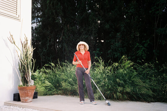 Senior Woman sweeping patio near green garden
