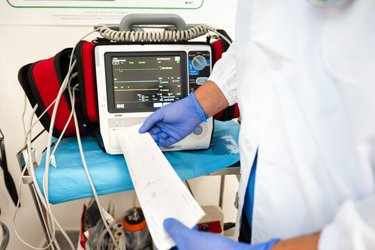 Paramedic reading electrocardiogram report next to defibrillator
