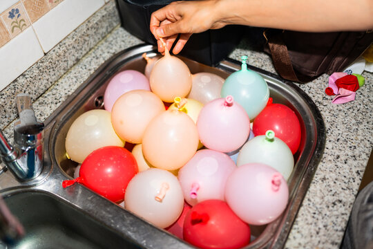 Woman preparing water balloons in kitchen sink for summer party