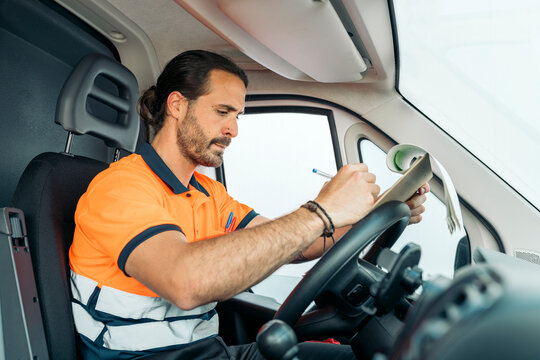 Logistic worker writing on clipboard inside van