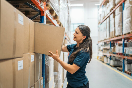 Female warehouse worker placing cardboard box on shelf