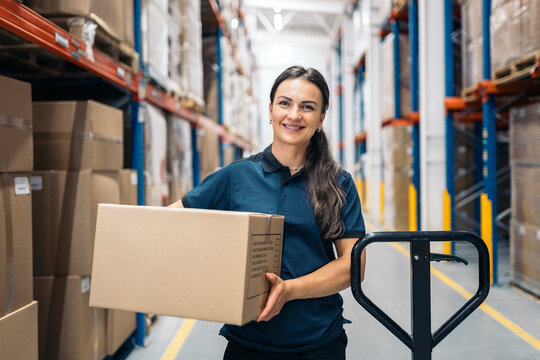 Smiling female worker carrying cardboard box in warehouse