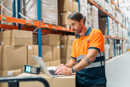 Logistic worker using laptop in warehouse with inventory